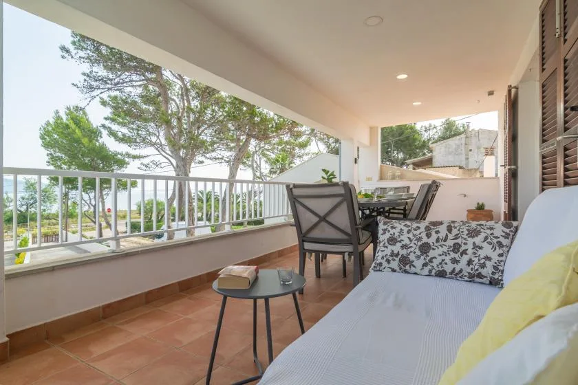 A covered terrace with seating, a table, and views of trees beyond the railing.