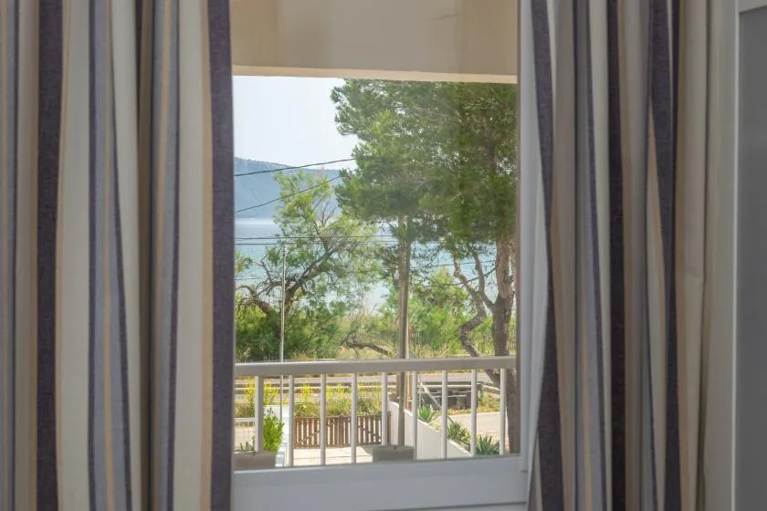 A curtained window overlooks trees, a railing, and water.