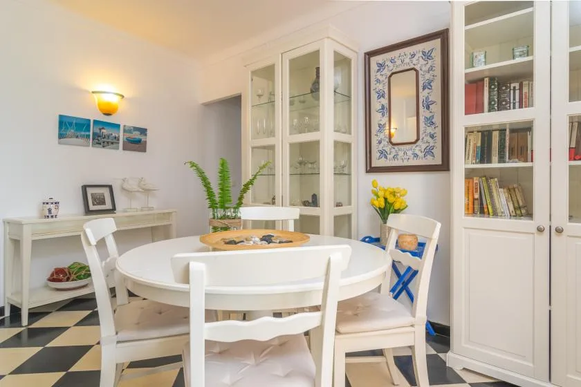 A bright dining area with a round table, white seating, and built-in shelves.