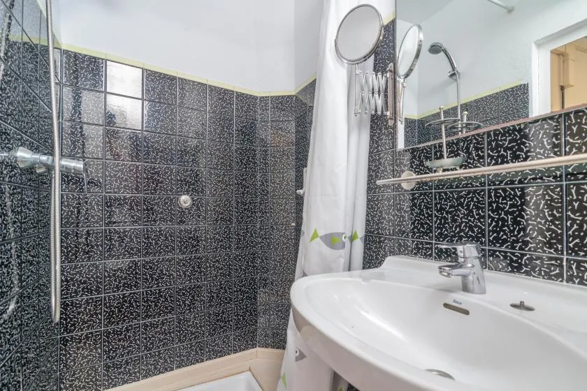 A bathroom with a curved sink, dark tiled walls, and a shower curtain.