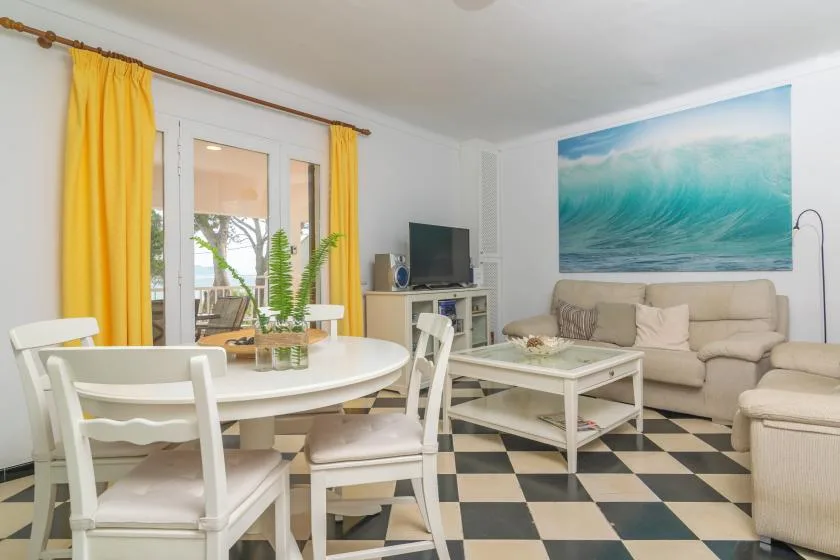 A living and dining room with white seating, a coffee table, and a large ocean-wave picture.