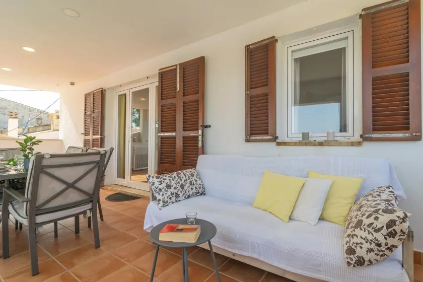 A covered patio seating area has a white sofa and a dining table.