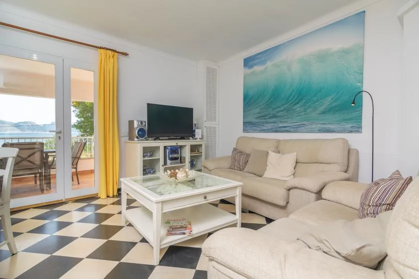 A living room with beige seating, a television, and a large ocean-wave artwork.