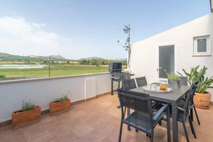 A terrace dining area with outdoor seating overlooks green fields and low hills.
