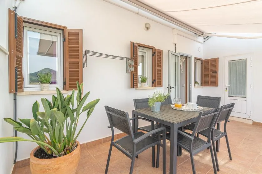 A dining area with a table and chairs sits beside shuttered windows.