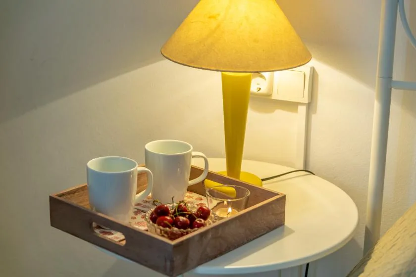 A bedside table holds a tray with two cups and a lit lamp.
