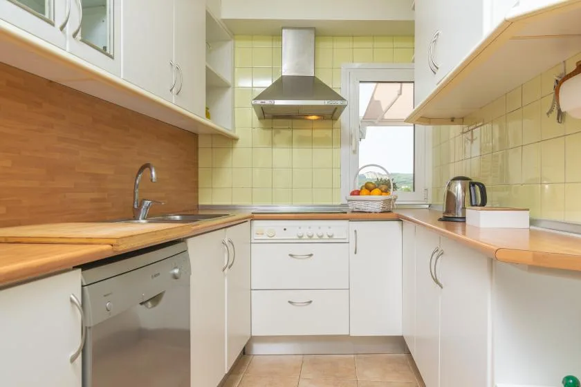 A bright kitchen with wood countertops, white cabinets, and a window above the sink.