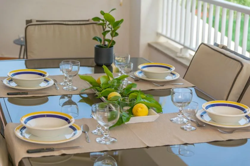 A dining table is set with plates, glasses, and a leafy centerpiece.