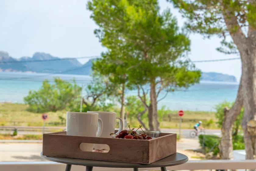 A wooden tray with cups and fruit sits on an outdoor table overlooking the water.