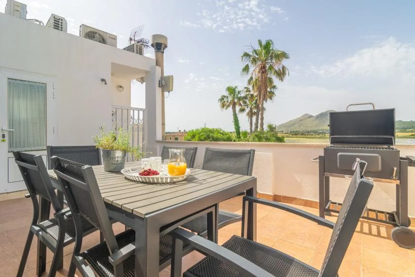 An outdoor dining area with a table, seating, and a barbecue on a sunny terrace.