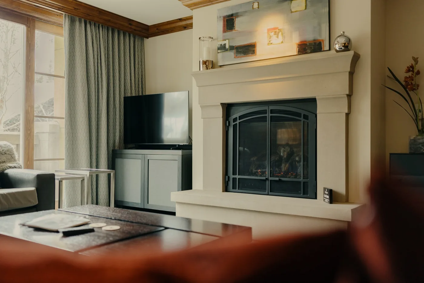 Una sala de estar con chimenea, televisor y grandes ventanas con cortinas.