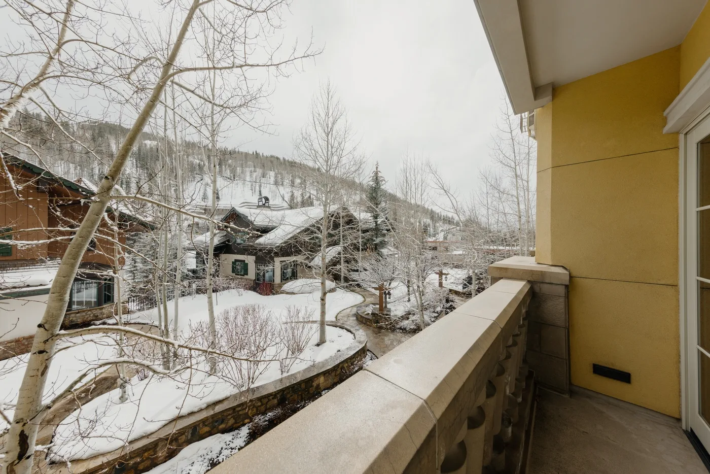 Un balcón da a una escena residencial nevada con árboles y edificios.