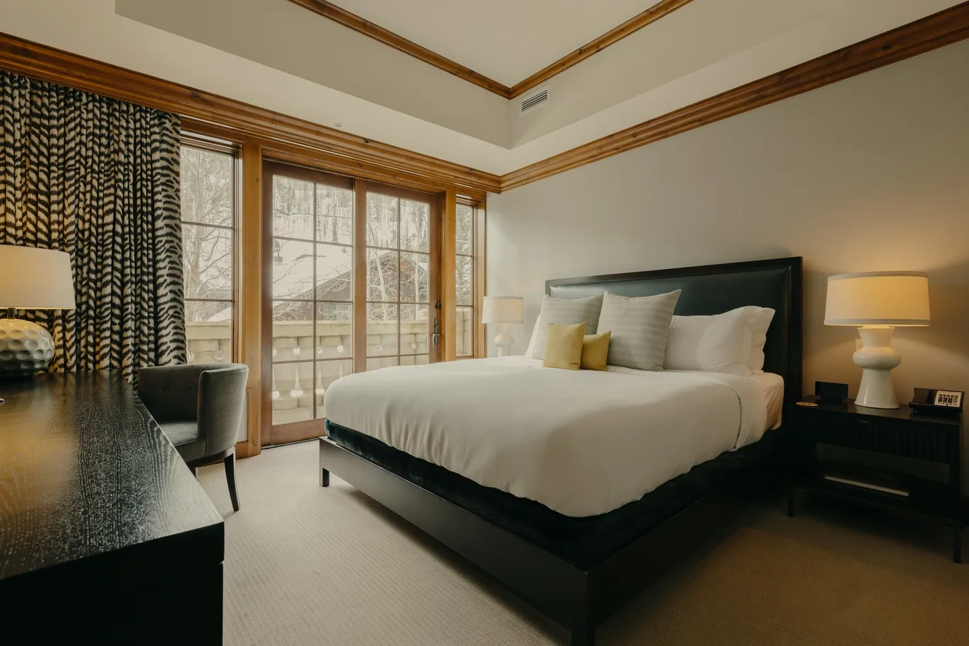Un dormitorio con una cama tendida, lámparas de noche y ventanas altas.