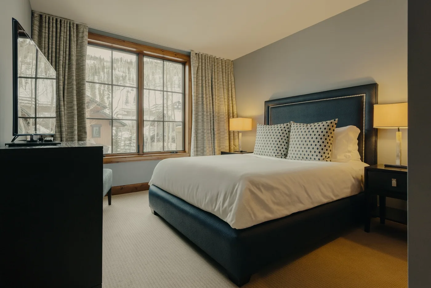 Un dormitorio con una cama bien tendida junto a una gran ventana con cortinas.