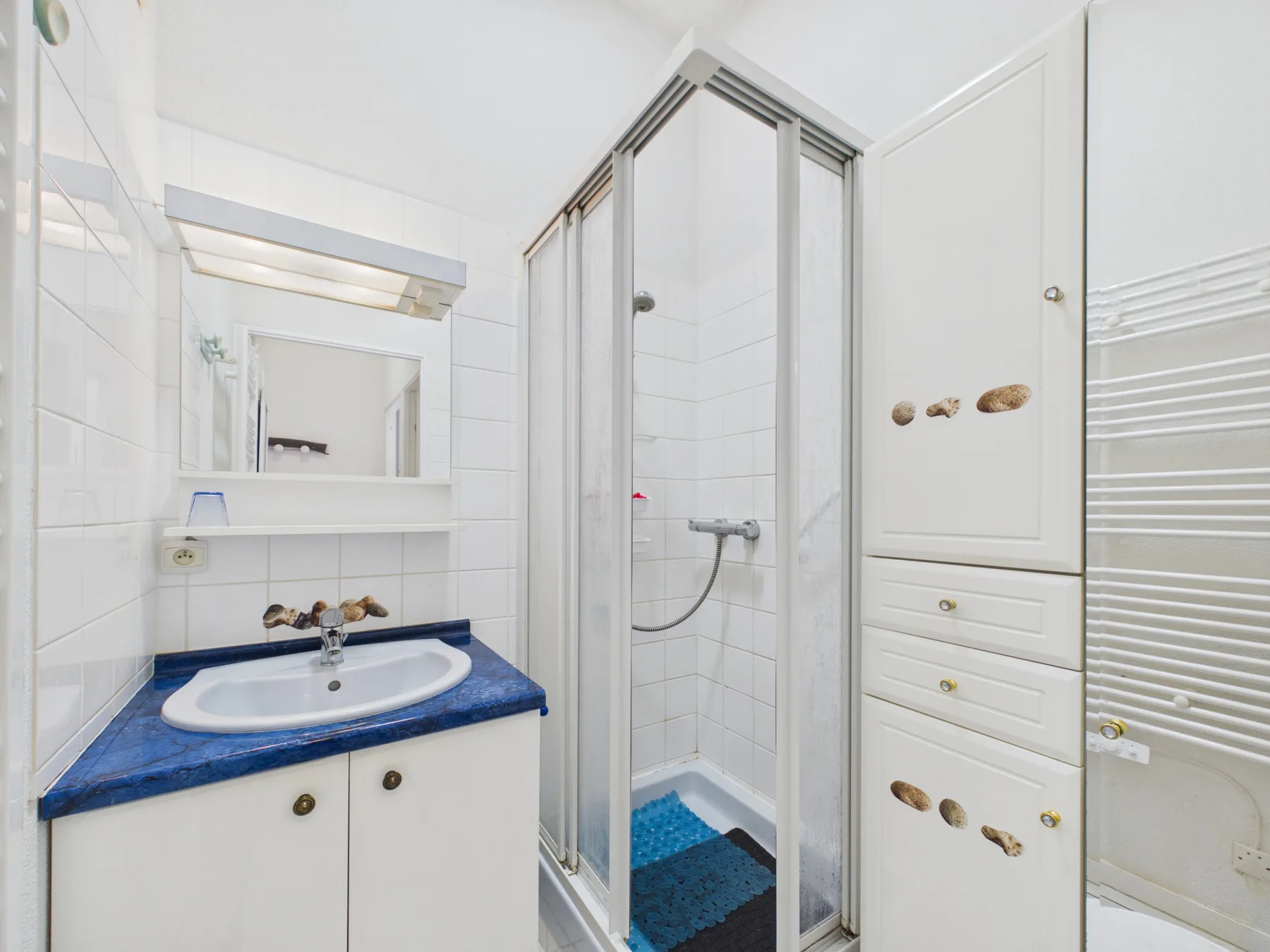 A white-tiled bathroom with a sink, shower, and built-in storage.