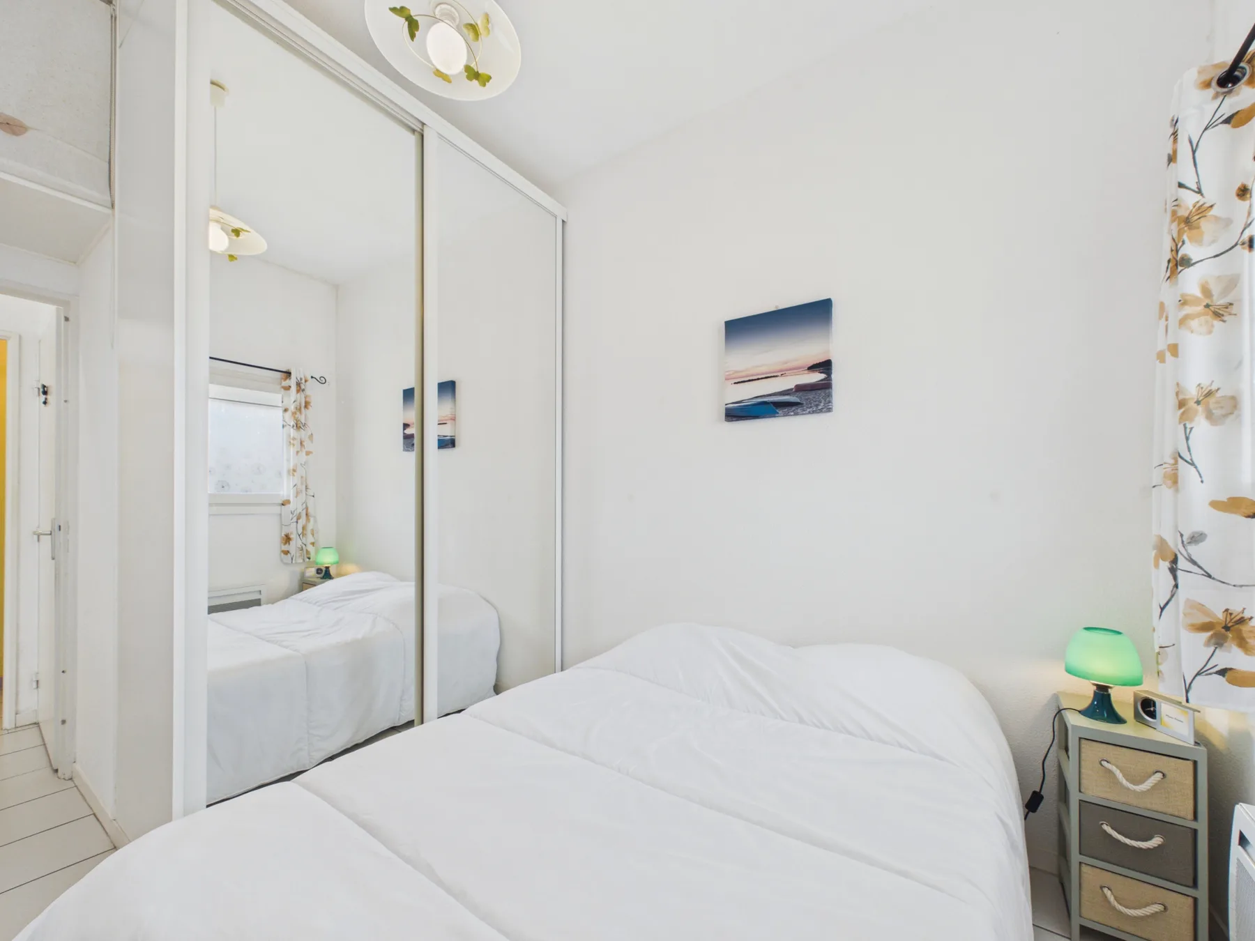 Bedroom with a bed, mirrored wardrobe, and a small bedside table.