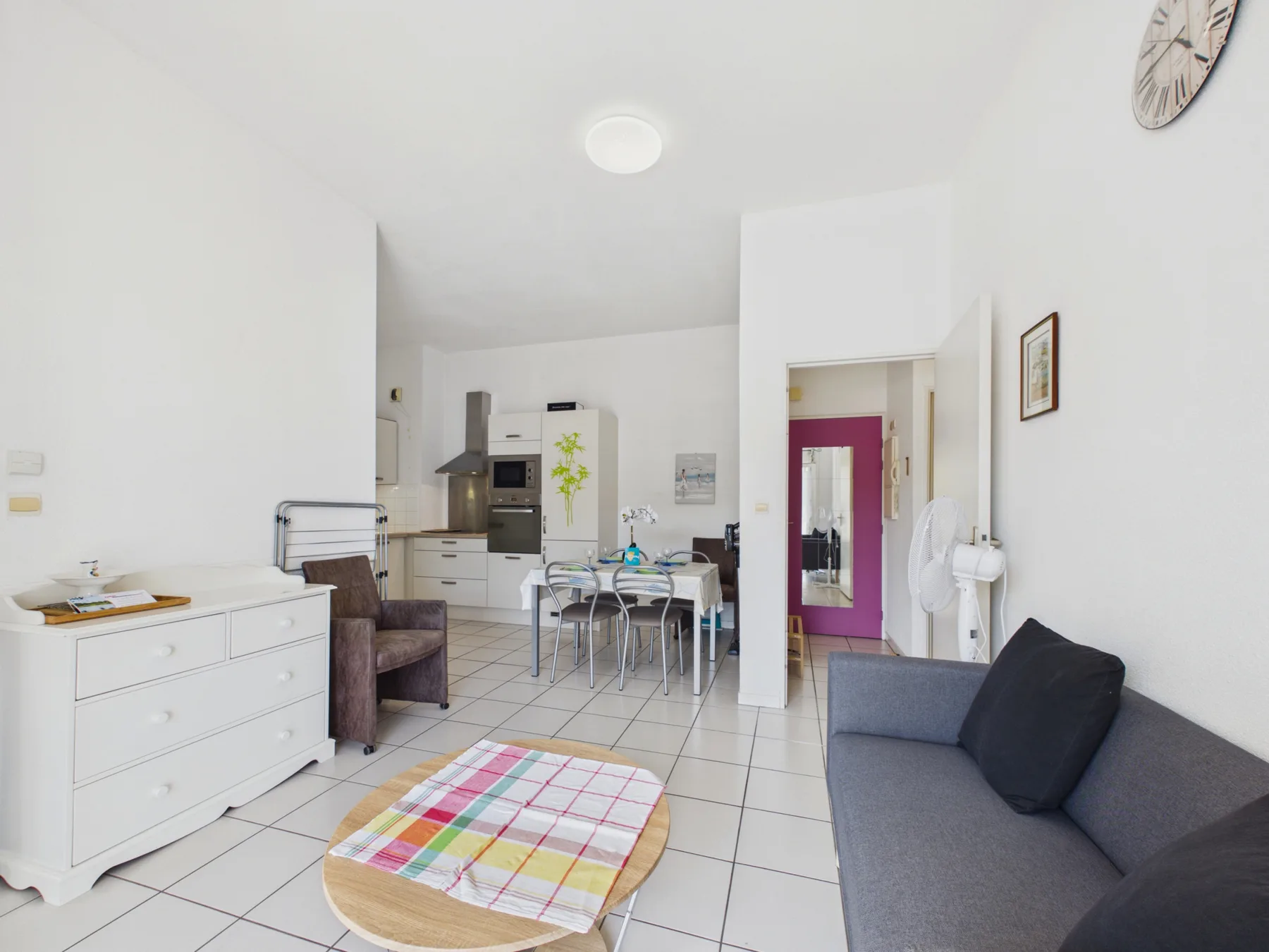 A bright apartment living area with seating and a dining table beside the kitchen.