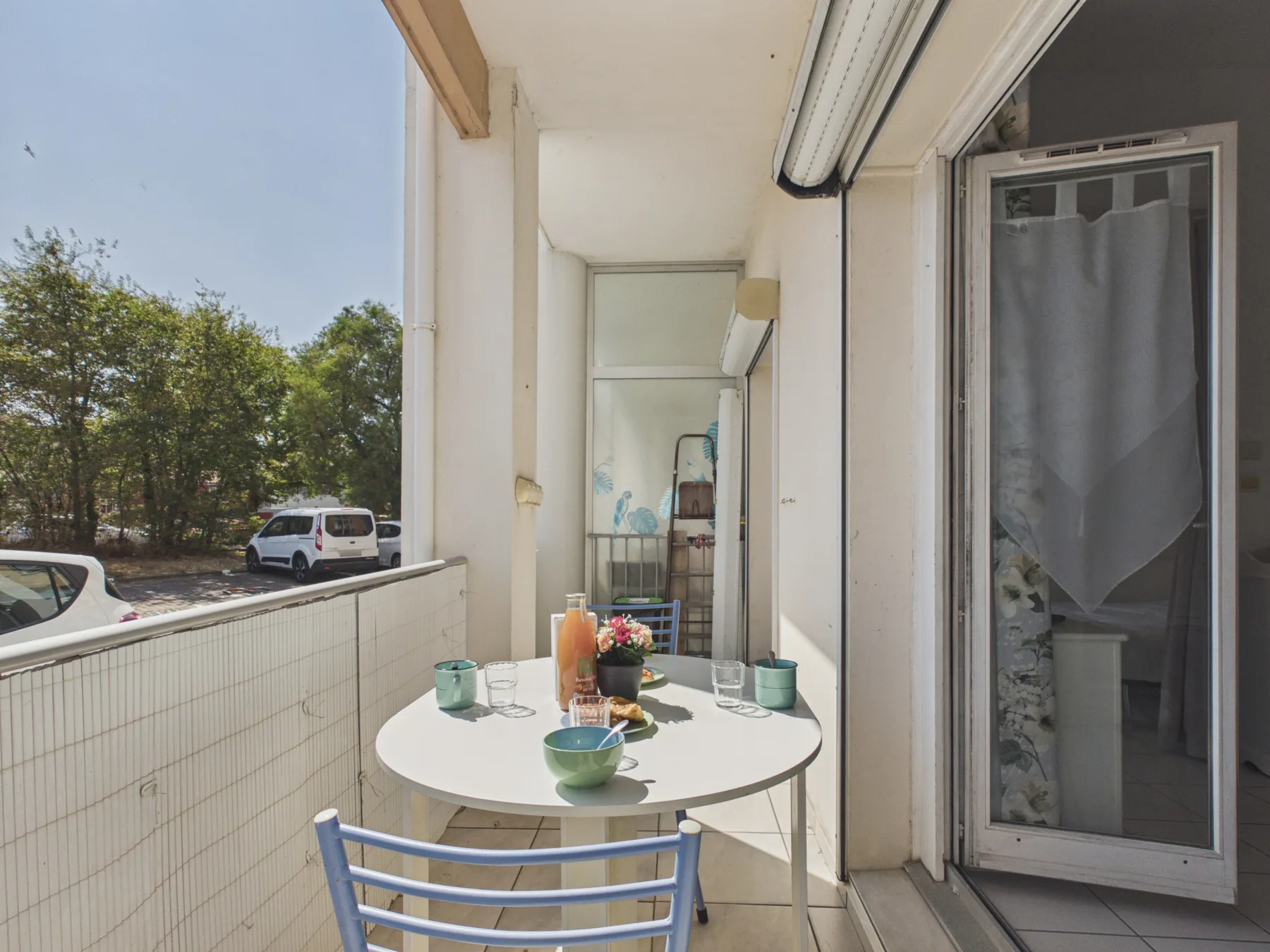 A covered balcony has a round table set with drinks and a small flower arrangement.