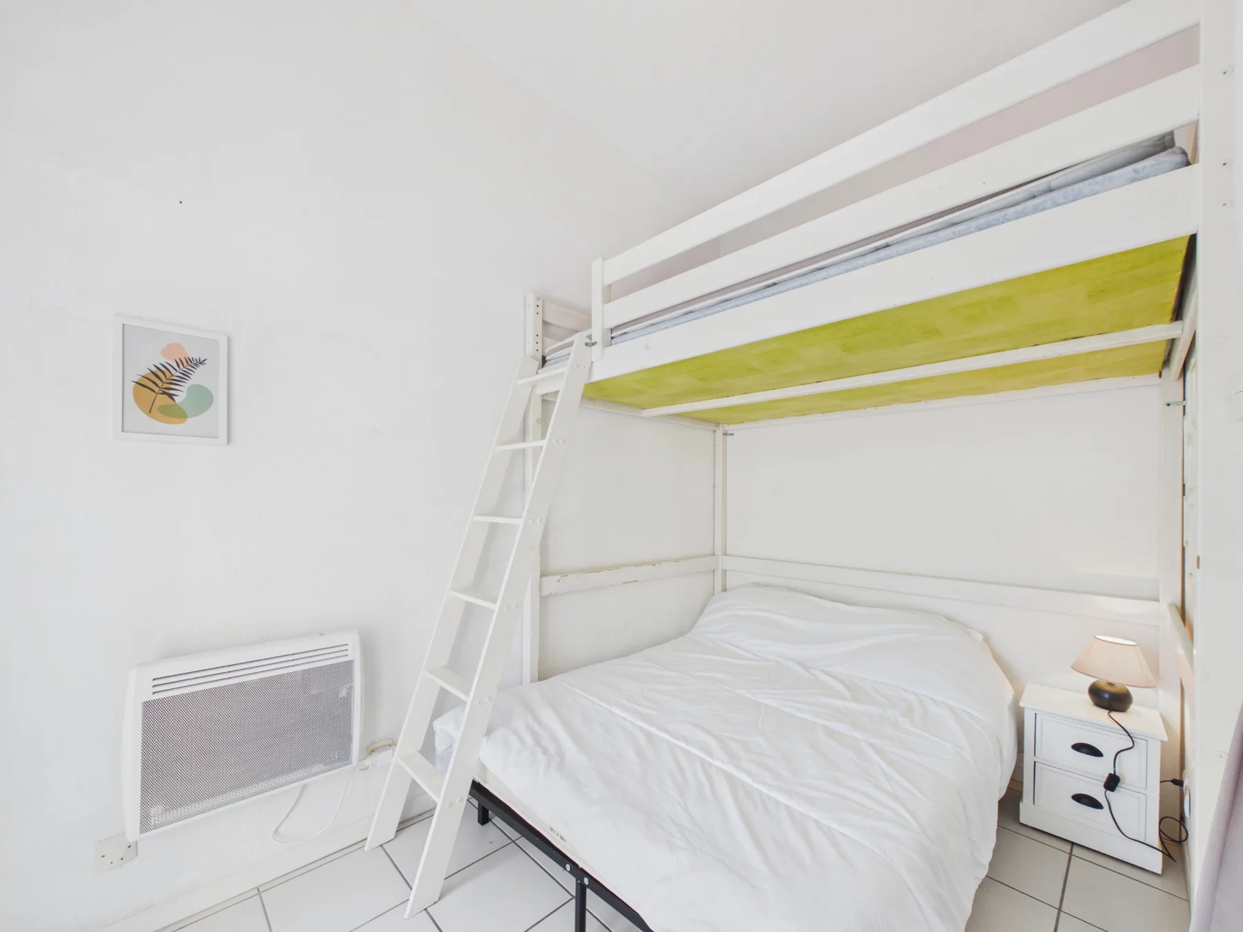 A bedroom with a bunk bed, a lower bed, and a small bedside table.