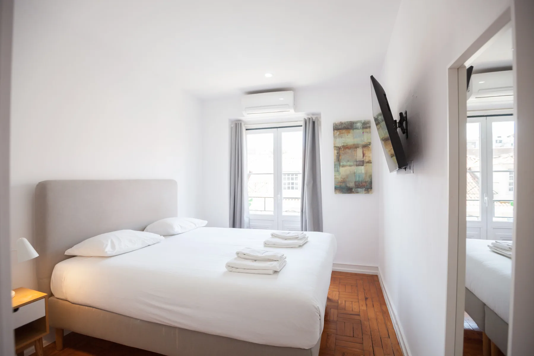 A bright bedroom with a neatly made bed, window, and wall-mounted television.