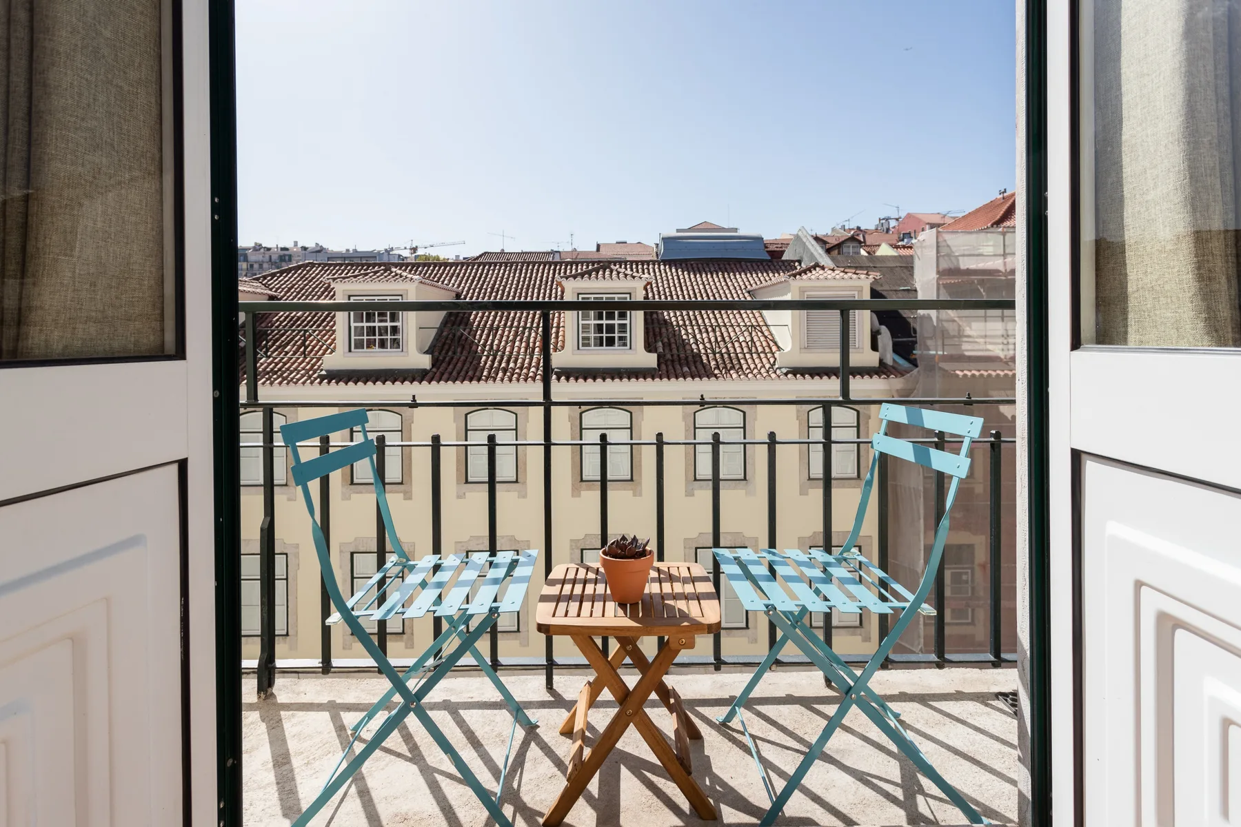 A small balcony with two chairs and a table overlooks tiled rooftops.
