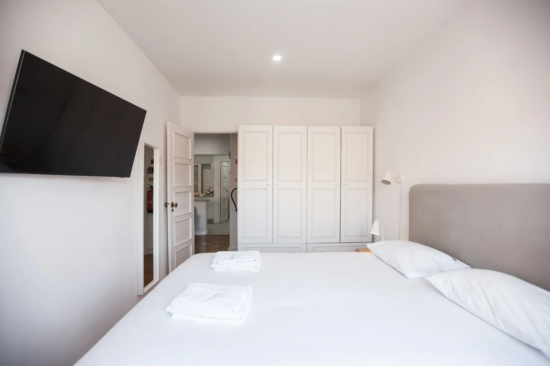 A bright bedroom with a large bed, wall-mounted television, and white wardrobes.