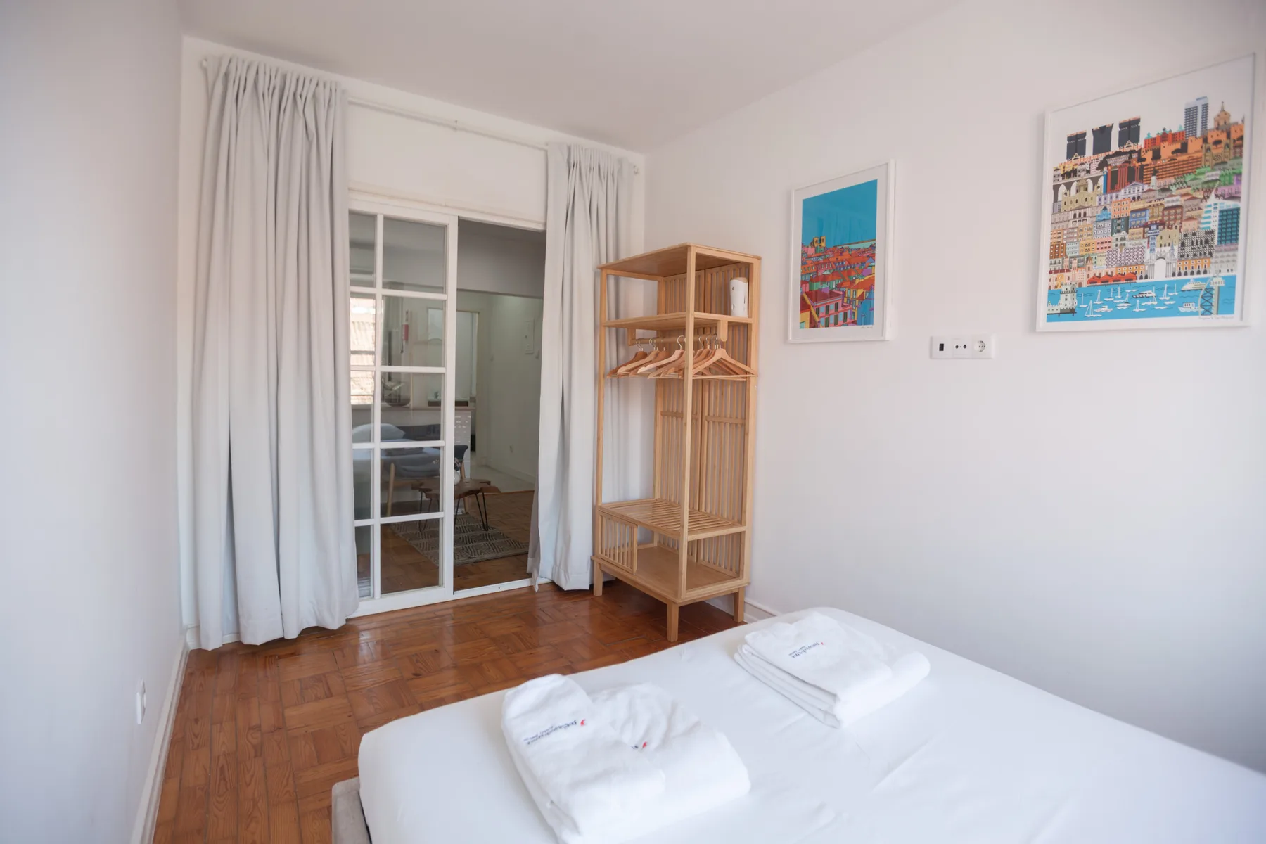 A bedroom with a bed, folded towels, and a curtained glass door.