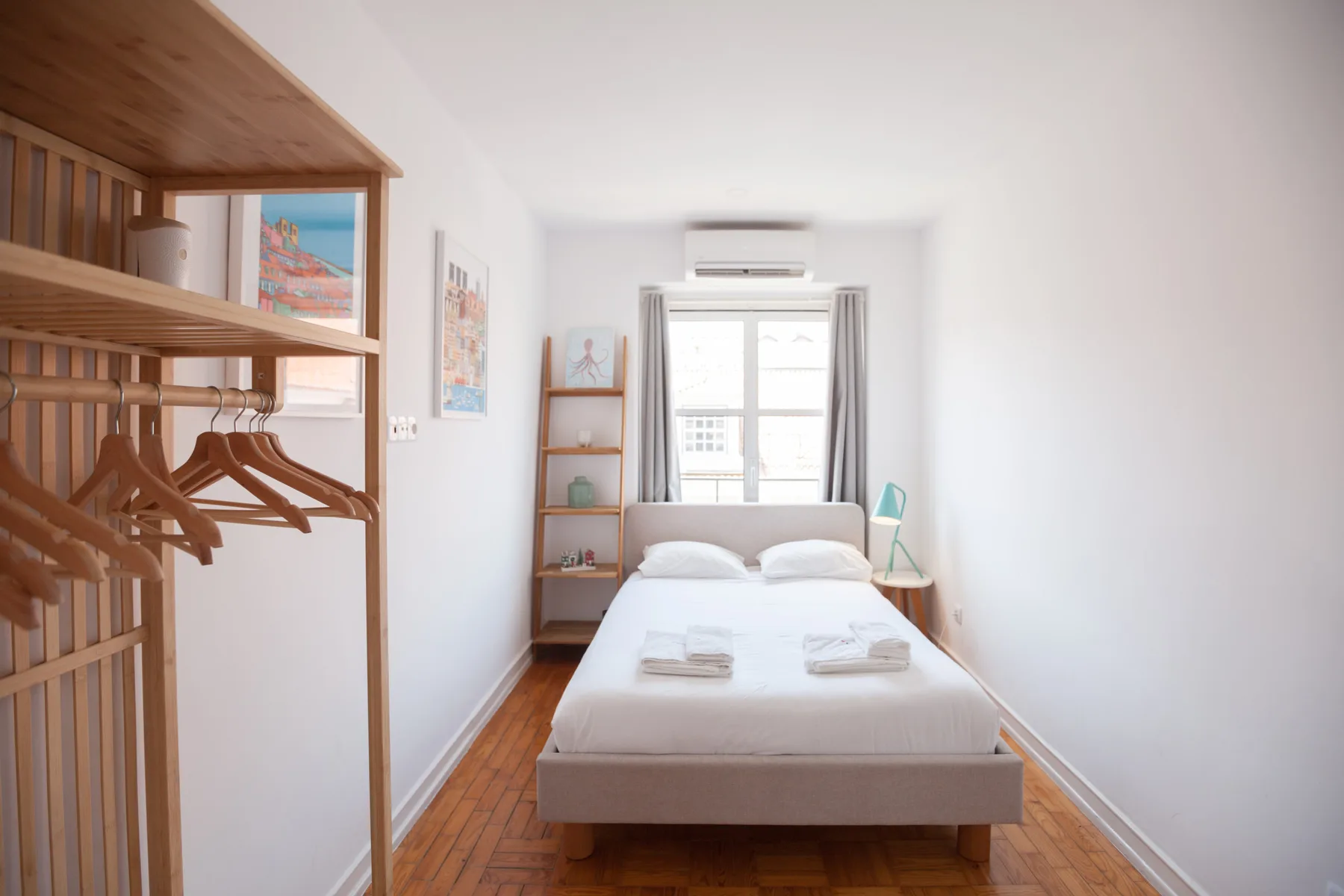 A bright bedroom with a bed, open clothing rack, and window.