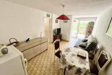 A bright living and dining room with seating, a television, and a table by the patio doors.