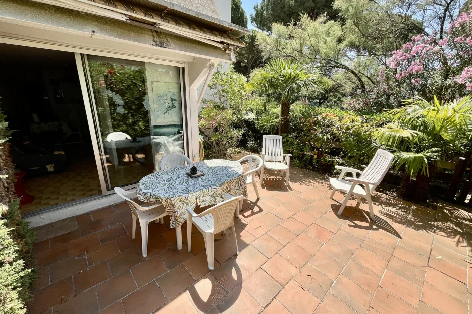 A tiled outdoor patio with a dining table, chairs, and surrounding greenery.