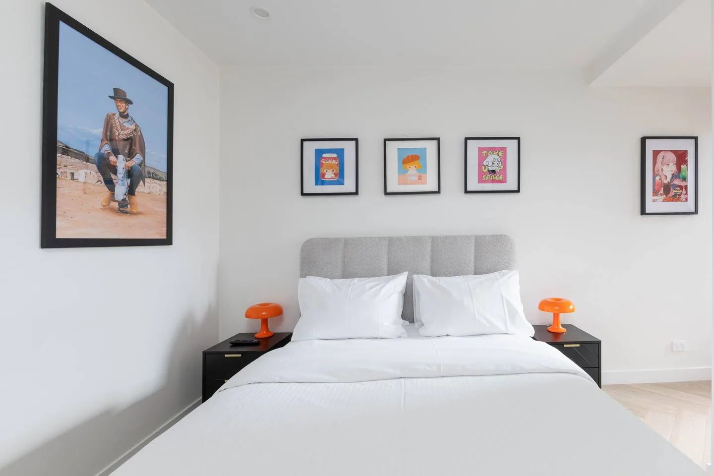 A bright bedroom with a bed, gray headboard, and framed artwork on the walls.