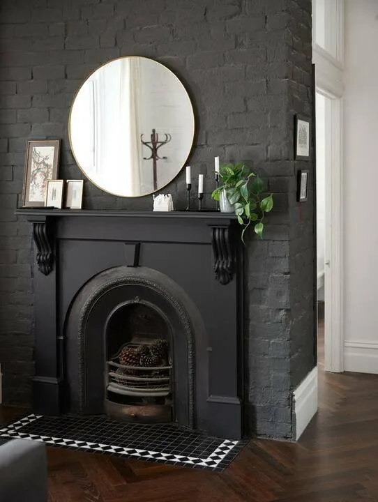 A dark fireplace set into a brick wall, with a round mirror above the mantel.