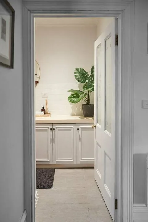 A bright bathroom vanity is visible through an open doorway, with a potted plant on the counter.