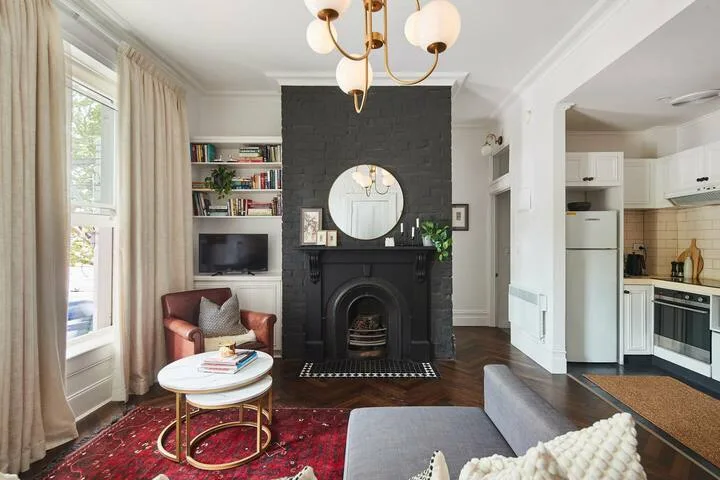 A living room with a dark fireplace, seating, and a small adjoining kitchen.