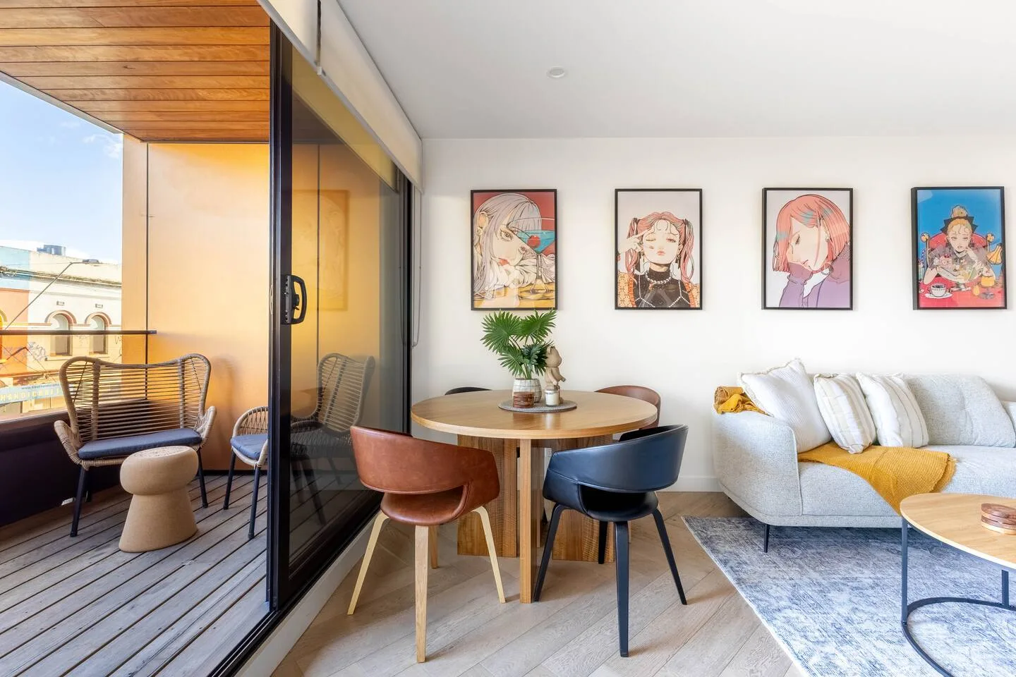 Comparte comidas en la mesa de comedor redonda de madera, situada junto a puertas de vidrio de suelo a techo que se abren al balcón, combinando la comodidad interior con el ambiente al aire libre.