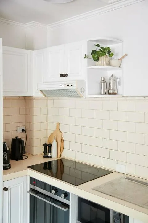 A bright kitchen with white cabinets, tiled walls, and a built-in cooktop and oven.