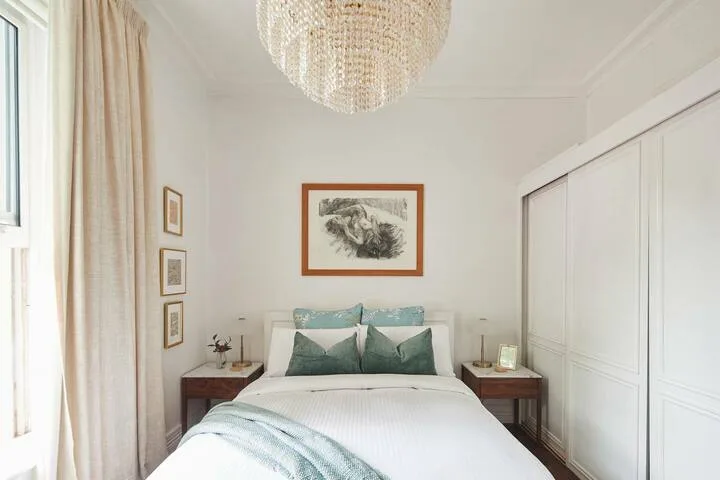 A bright bedroom with a double bed, bedside tables, and framed artwork.