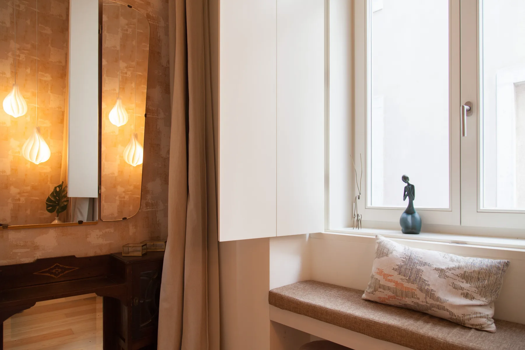 Un rincón luminoso junto a la ventana con asiento acolchado y tocador con espejo.