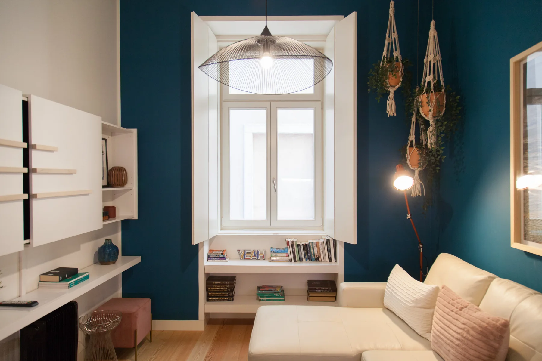 Una sala de estar con sofá, estantes empotrados y una ventana frente a una pared verde azulado.