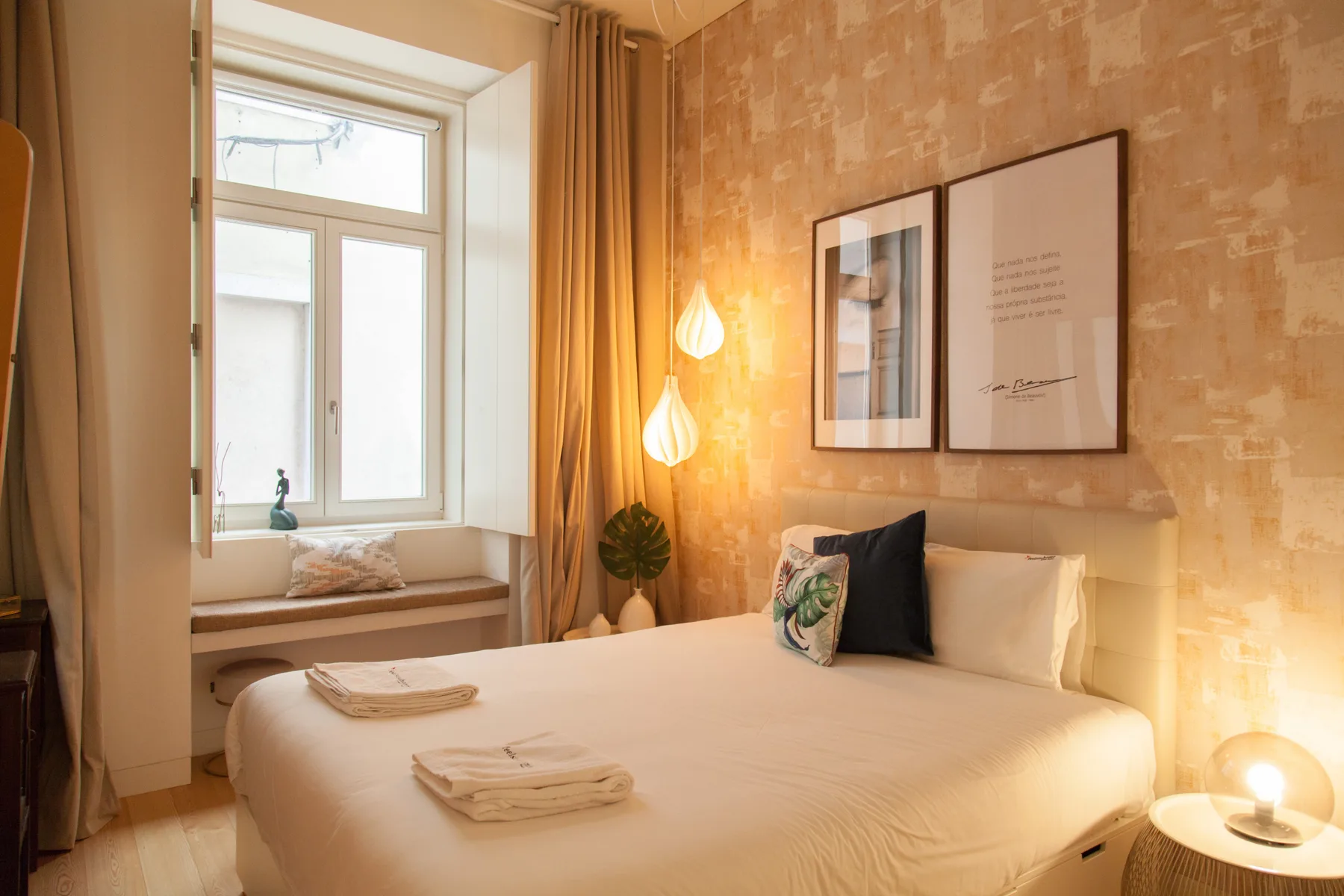 Un dormitorio con luz suave y una cama bien arreglada junto a una ventana grande.