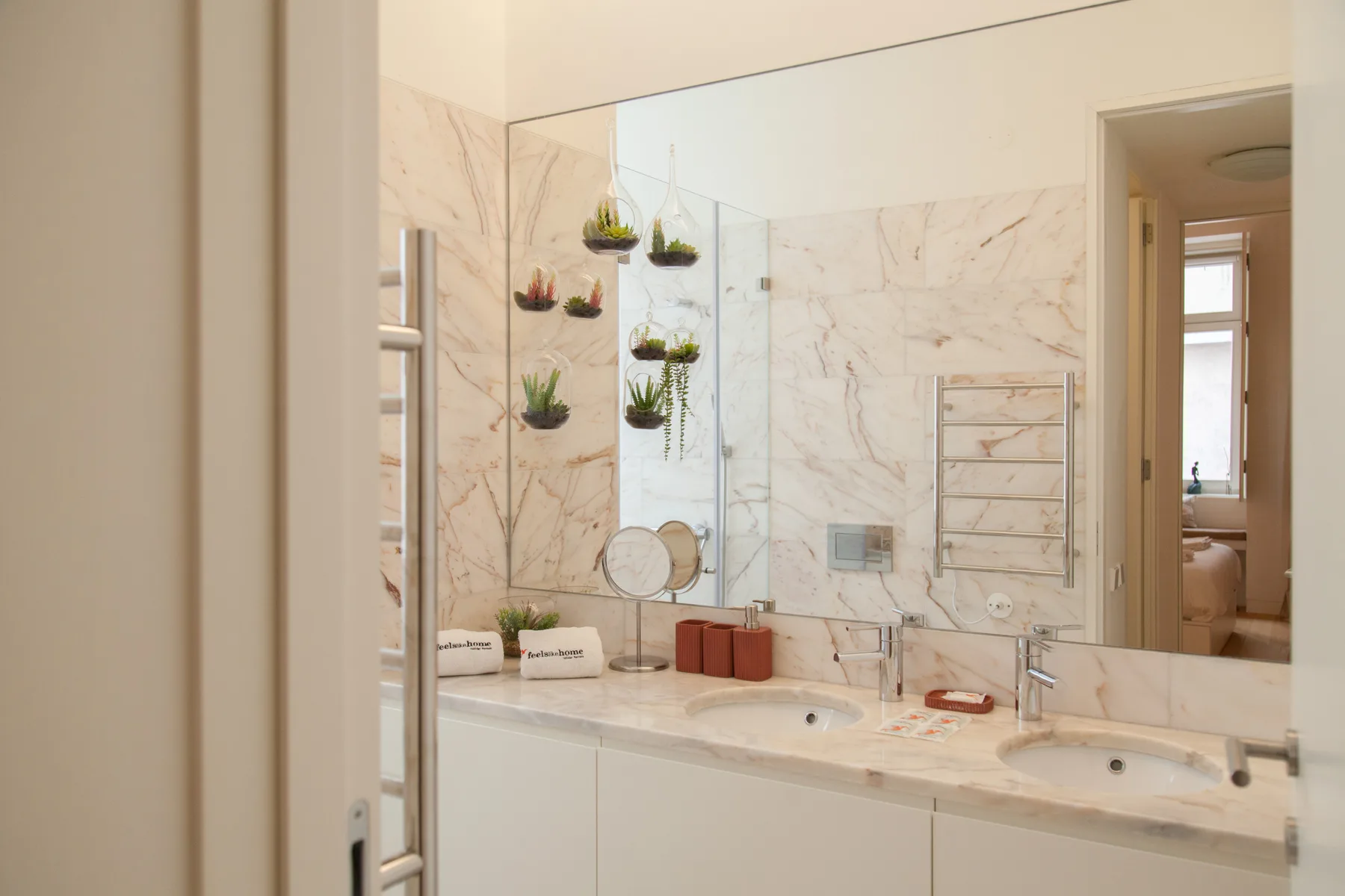 Un baño luminoso con un espejo amplio, paredes veteadas y dos lavabos.