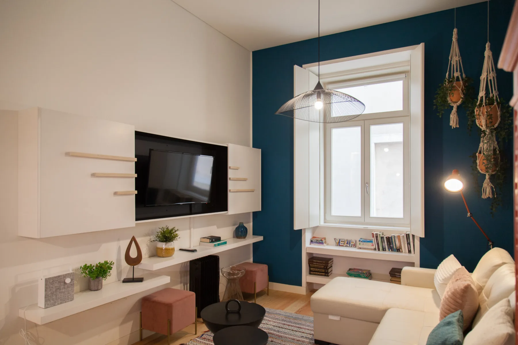 Una sala de estar con televisor montado en la pared, asientos y una ventana grande.