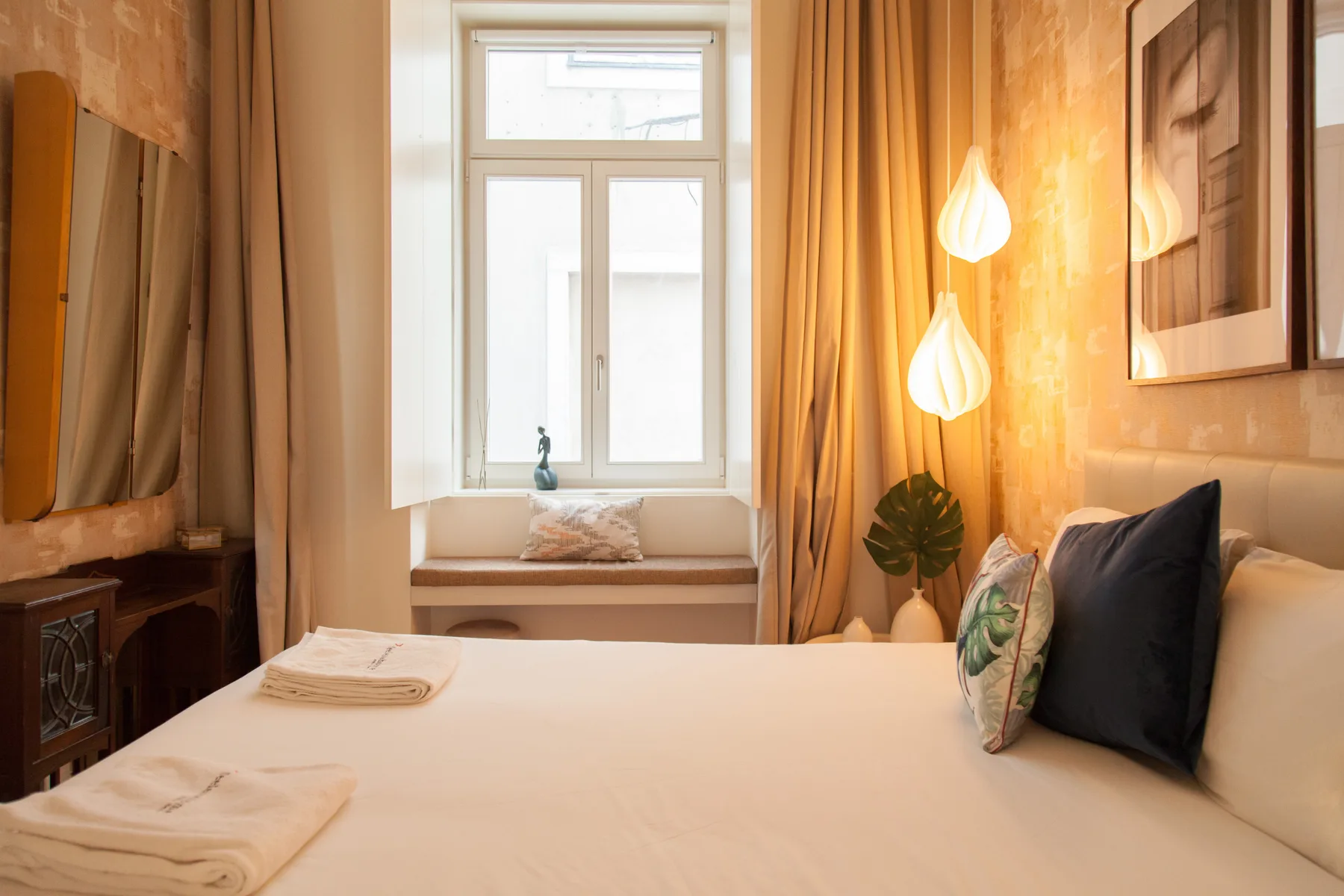 Un dormitorio con una cama bien hecha, almohadas y un asiento junto a la ventana.