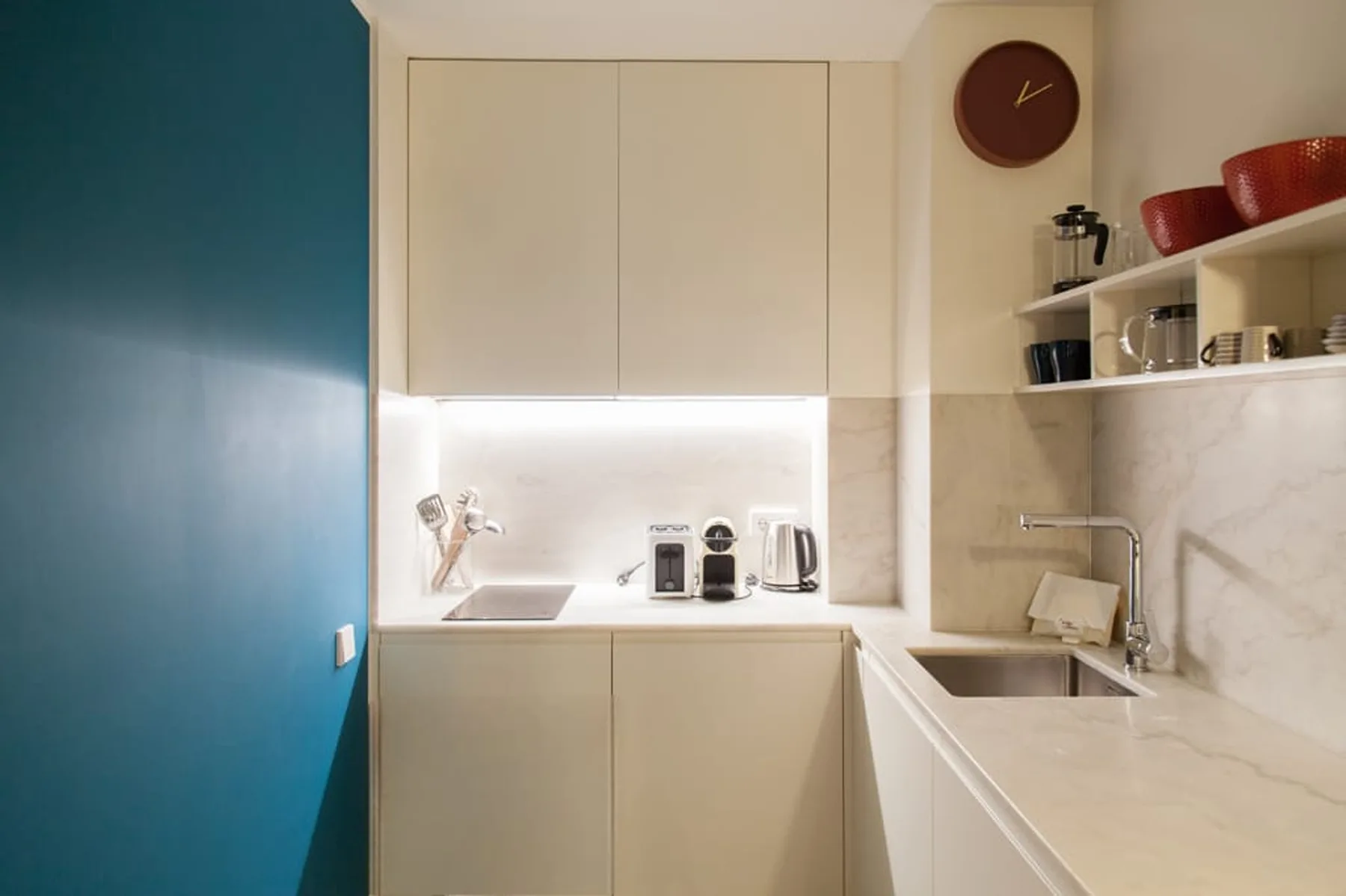 Una cocina compacta con armarios claros, fregadero y estantes abiertos.