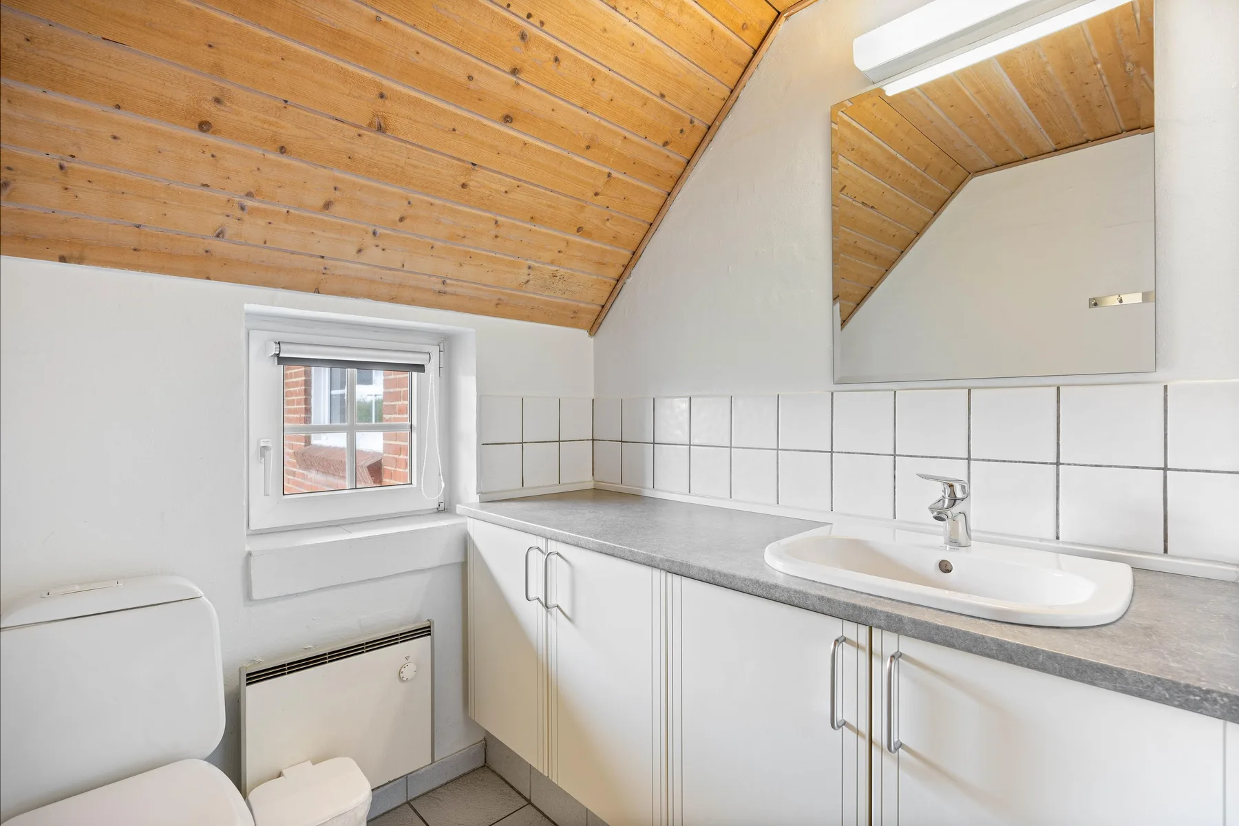 A bright bathroom with a tiled vanity, mirror, and sloped wooden ceiling.