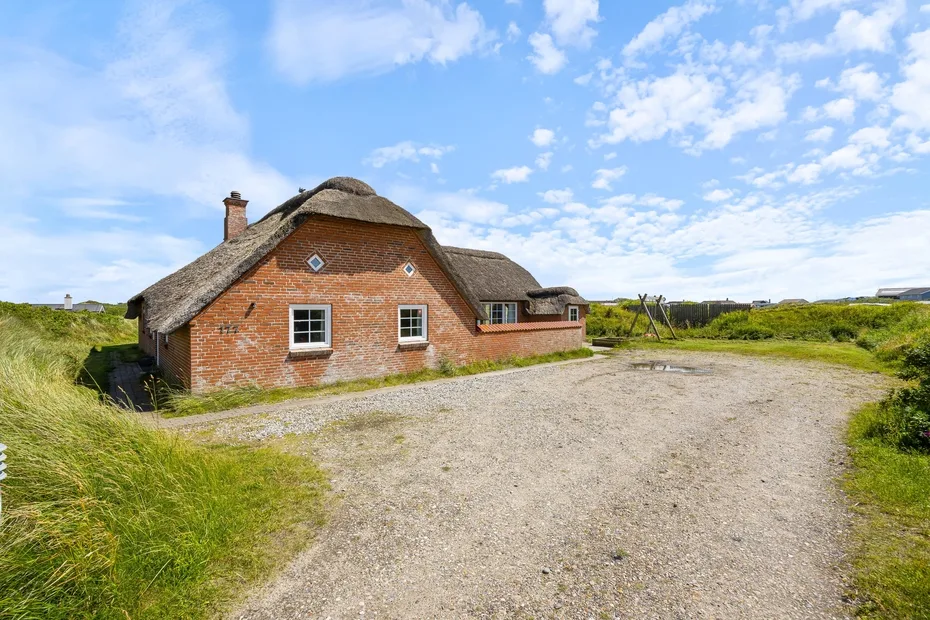 A brick house with a thatched roof stands beside a gravel drive in open grassland.