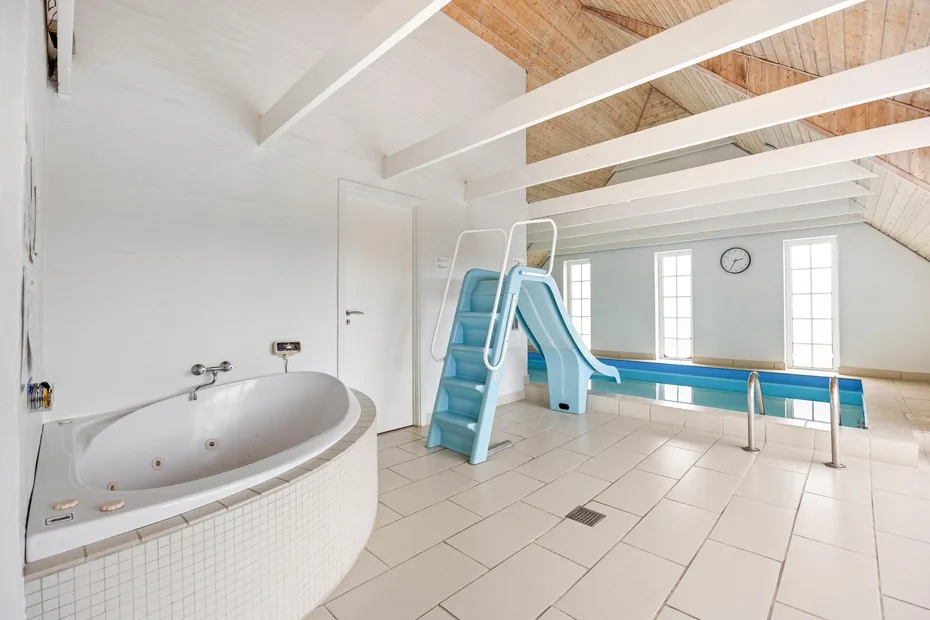 An indoor pool area with a blue slide and a built-in bathtub.