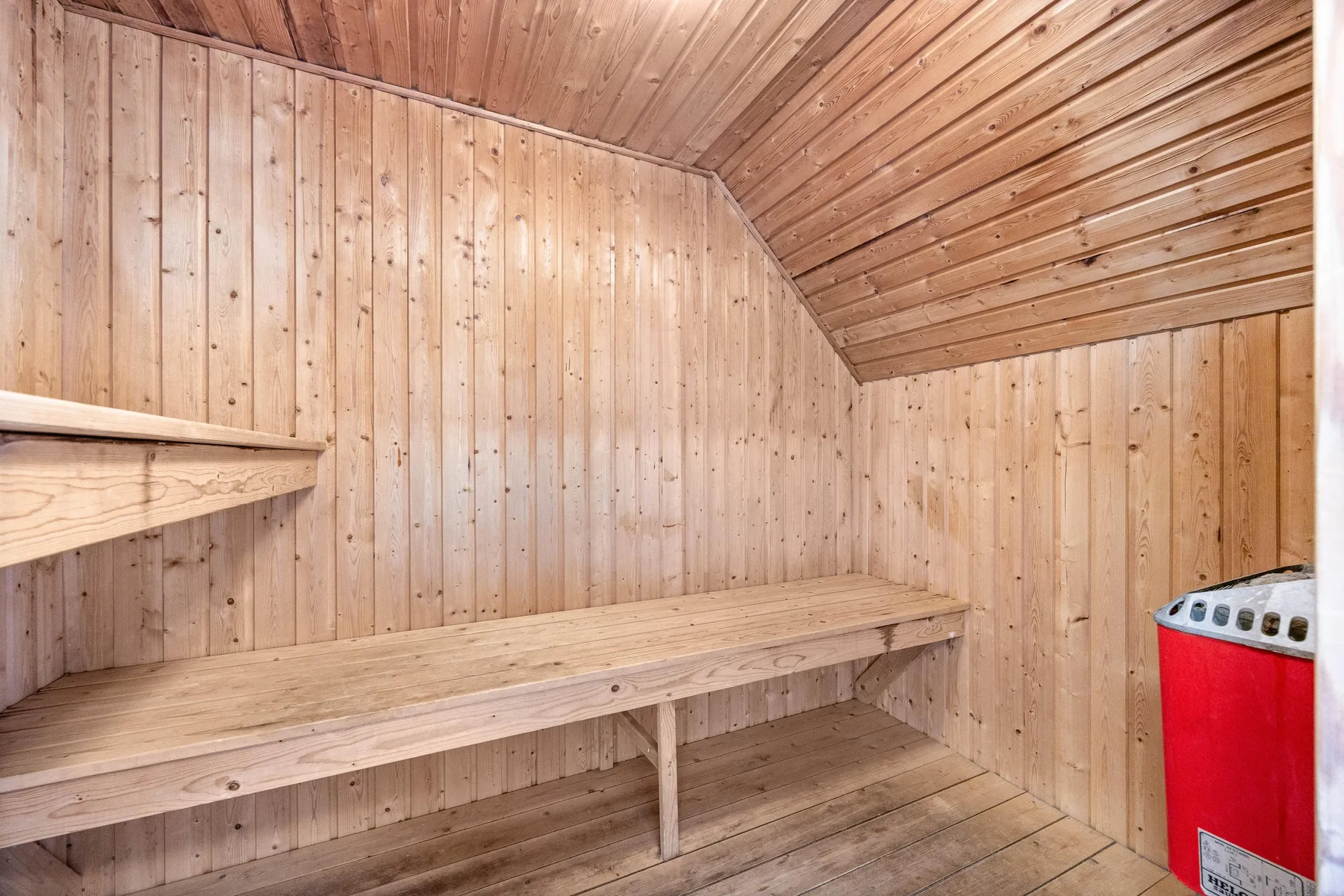 A wood-paneled sauna room with tiered wooden seating and a red heater.
