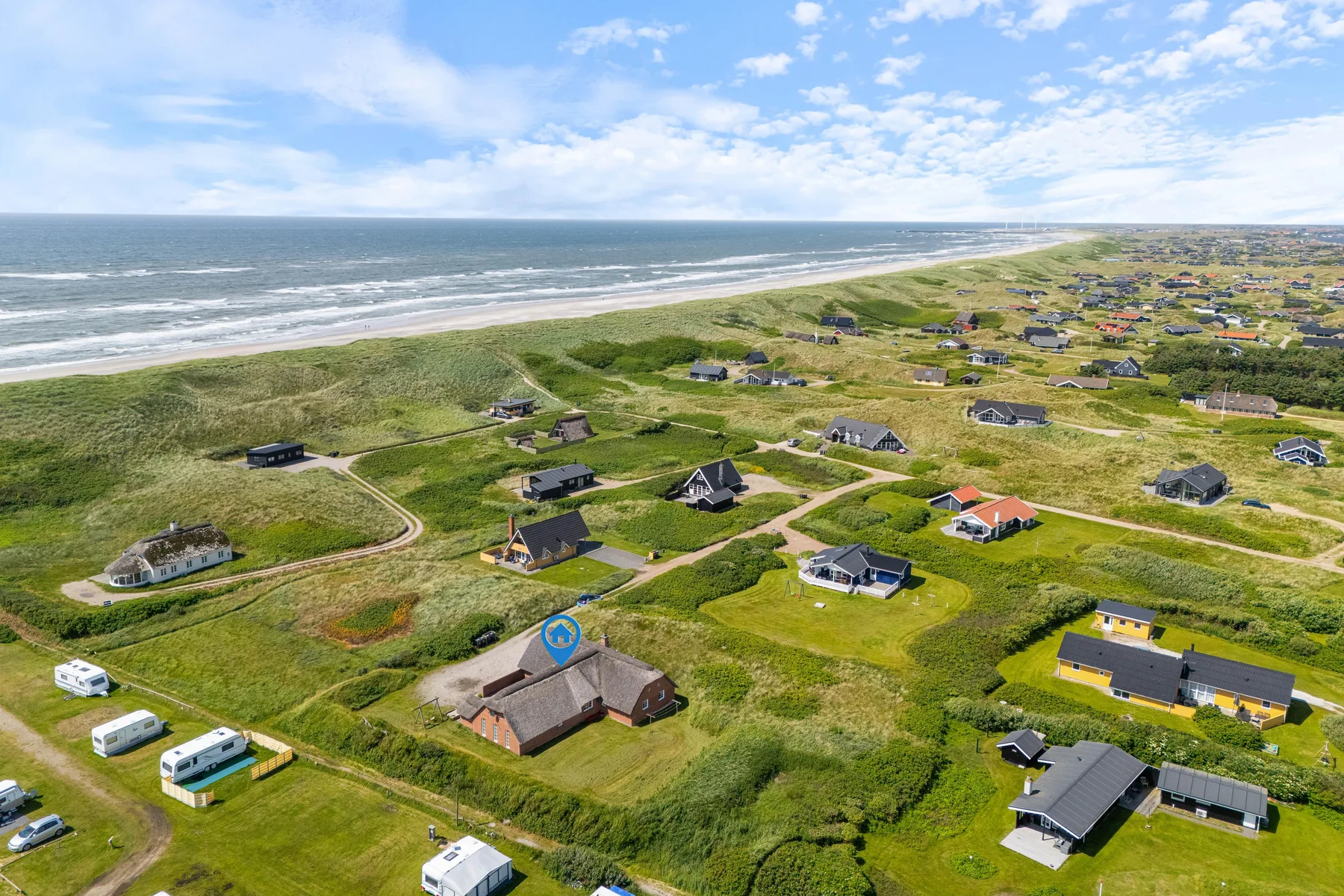 Aerial view of coastal homes and roads beside a grassy shoreline.