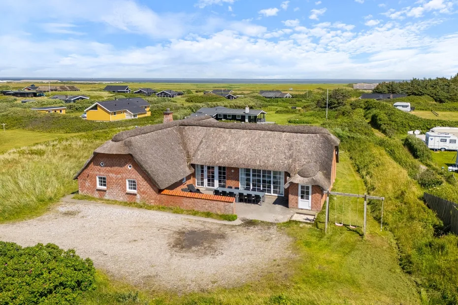 A thatched-roof building stands beside a gravel drive amid grassy grounds.